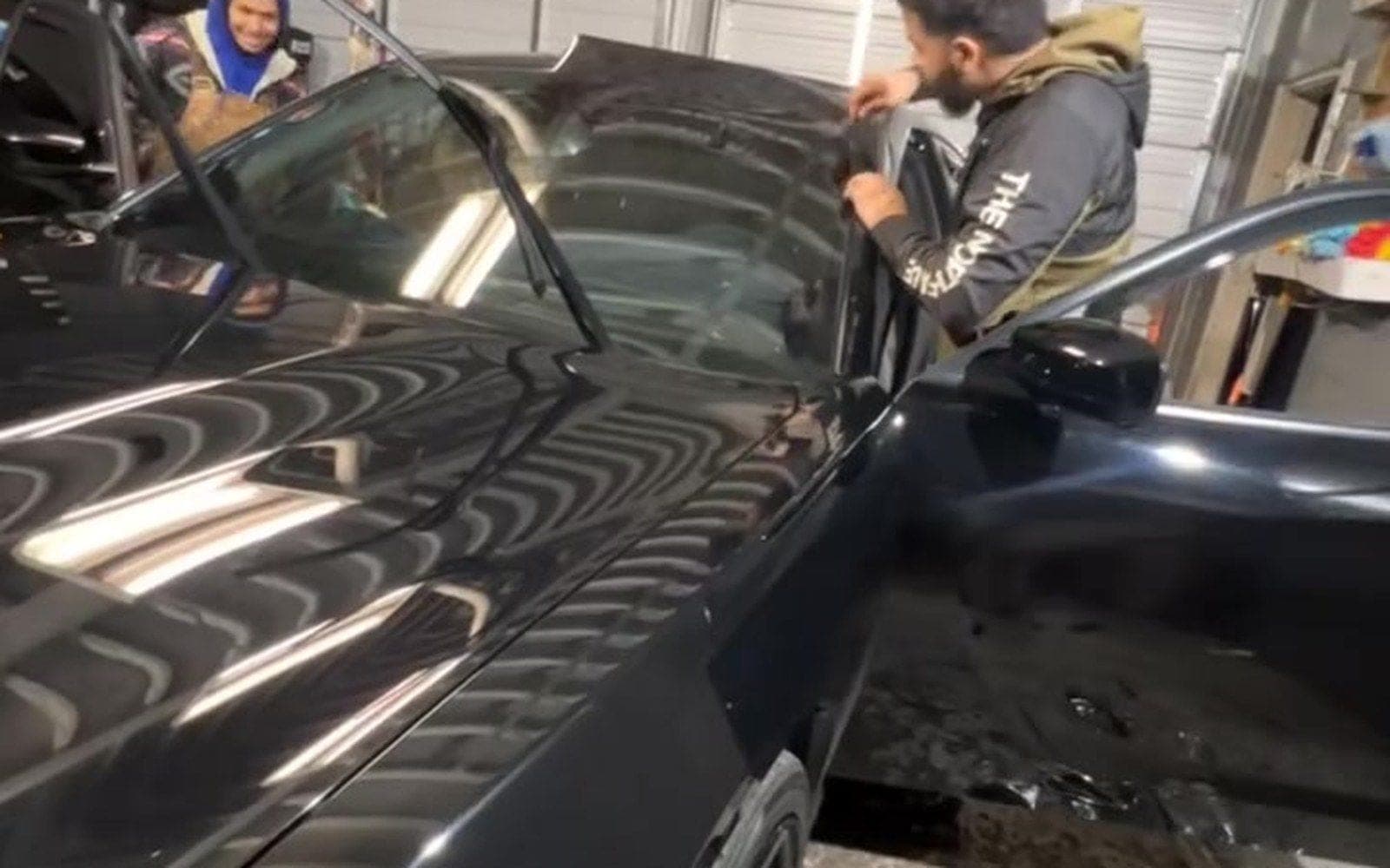 Two technicians laying film on a black car inside the shop